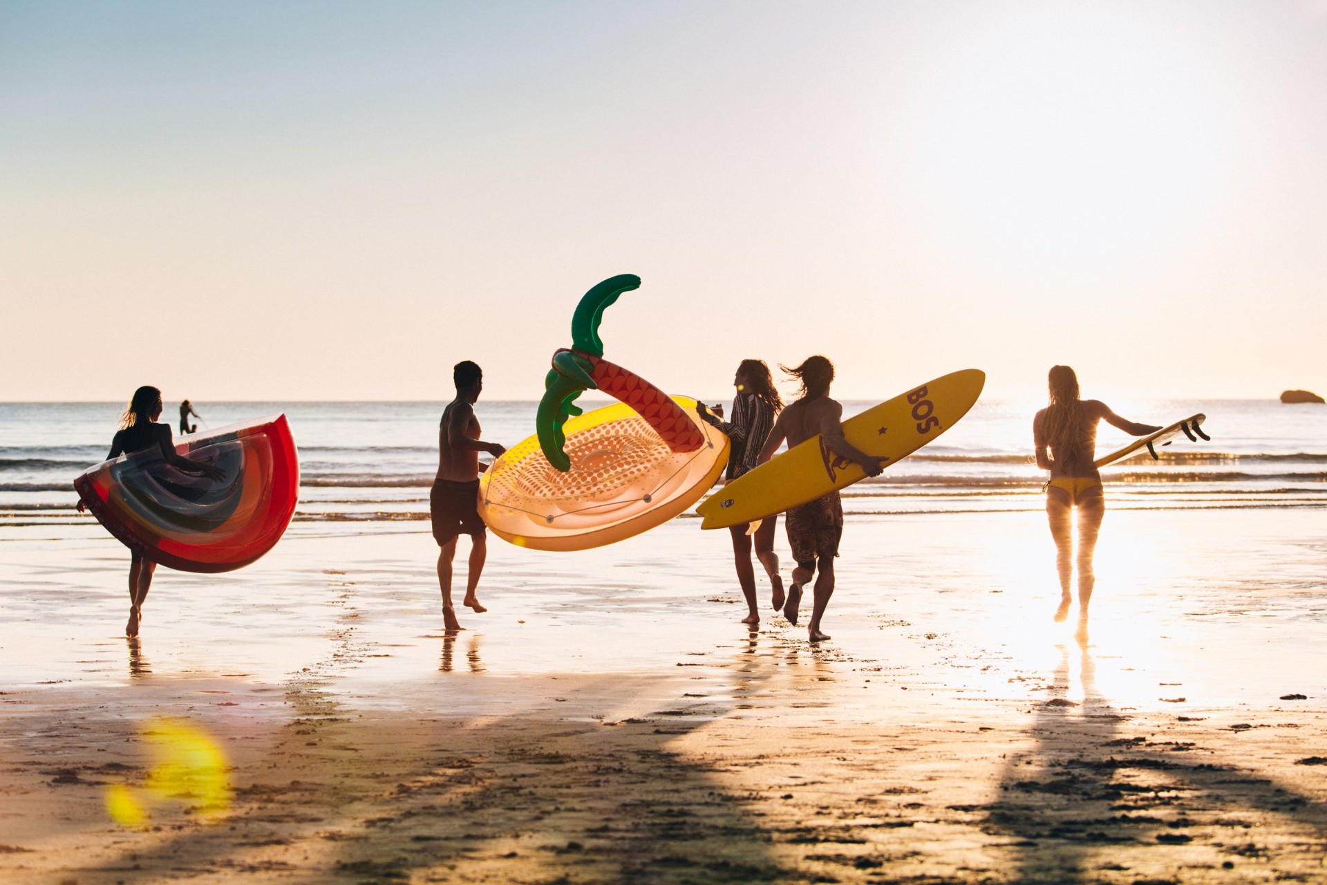 Friends running into the surf at sunset with a BOS surfboard and inflatable floats
