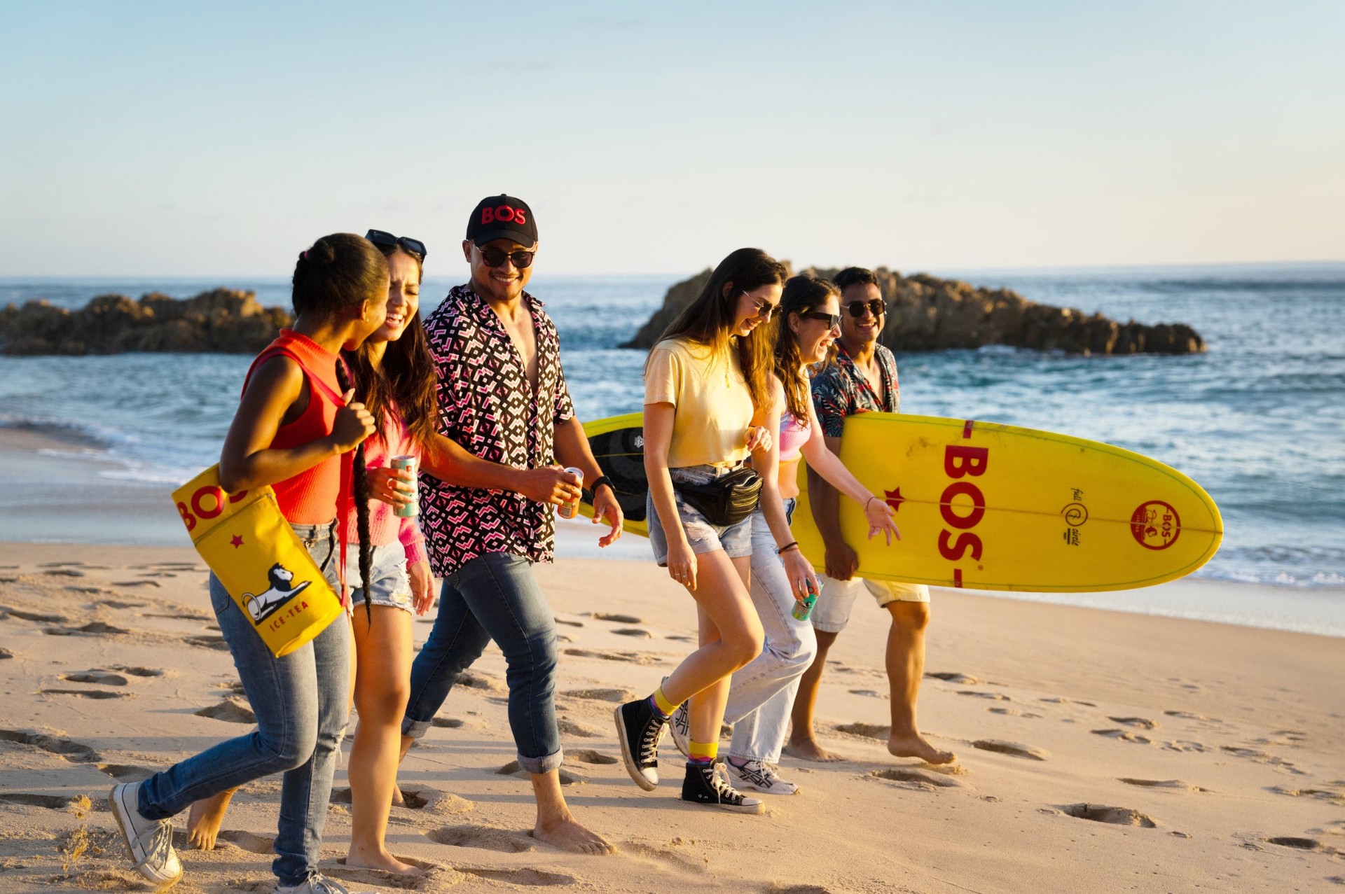 Group of friends walking on the beach with BOS surfboards and a yellow BOS cooler bag