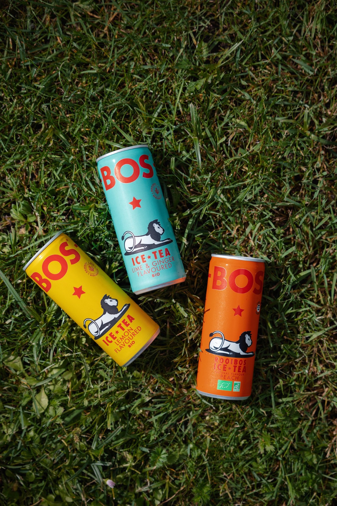BOS Lemon, Lime & Ginger and Peach rooibos cans laid on fresh green grass