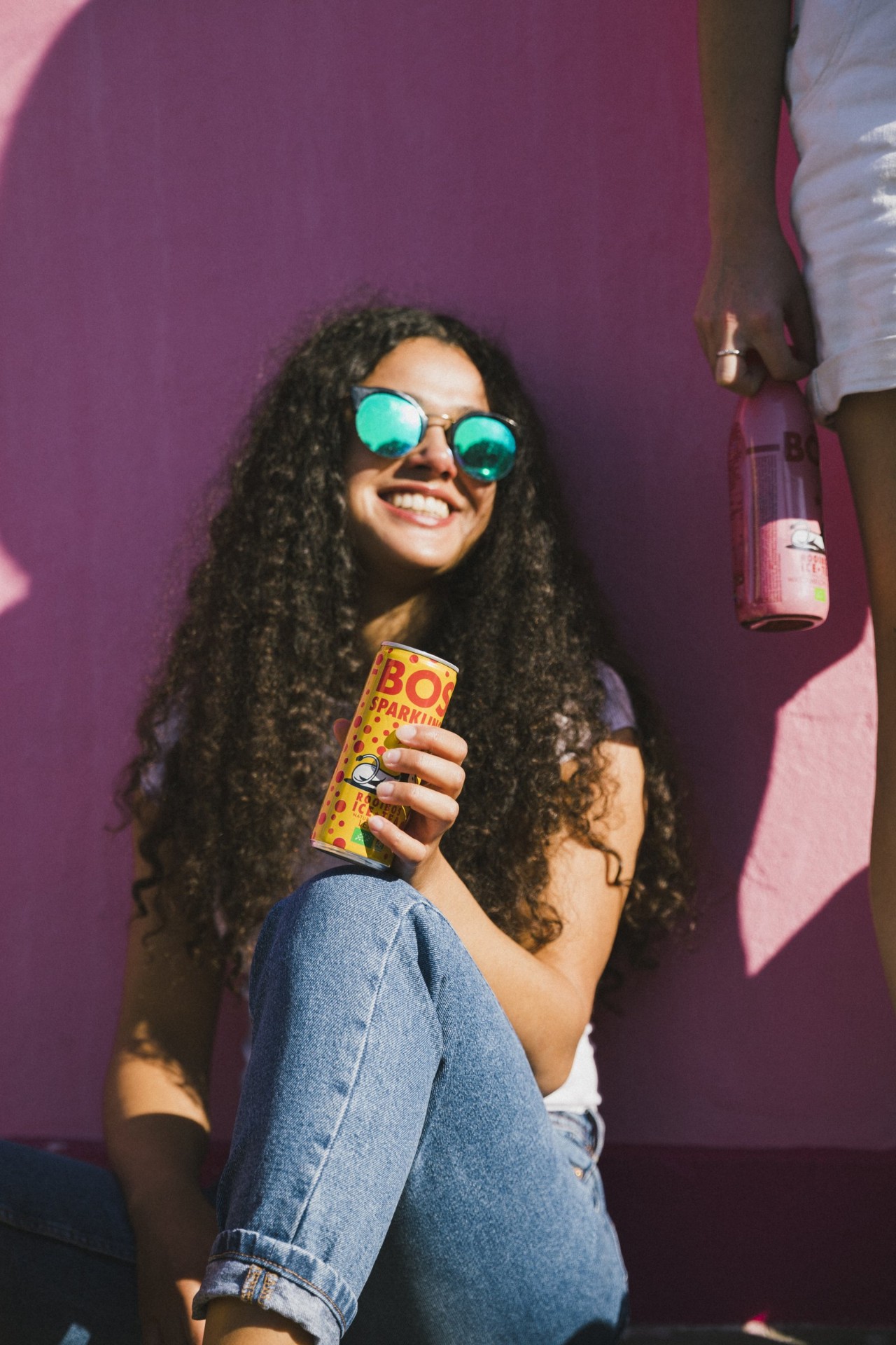 Woman in sunglasses holding a BOS can against a bright pink wall